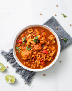 A vertical shot of chickpea curry chana masala with lime in a bowl on a white surf